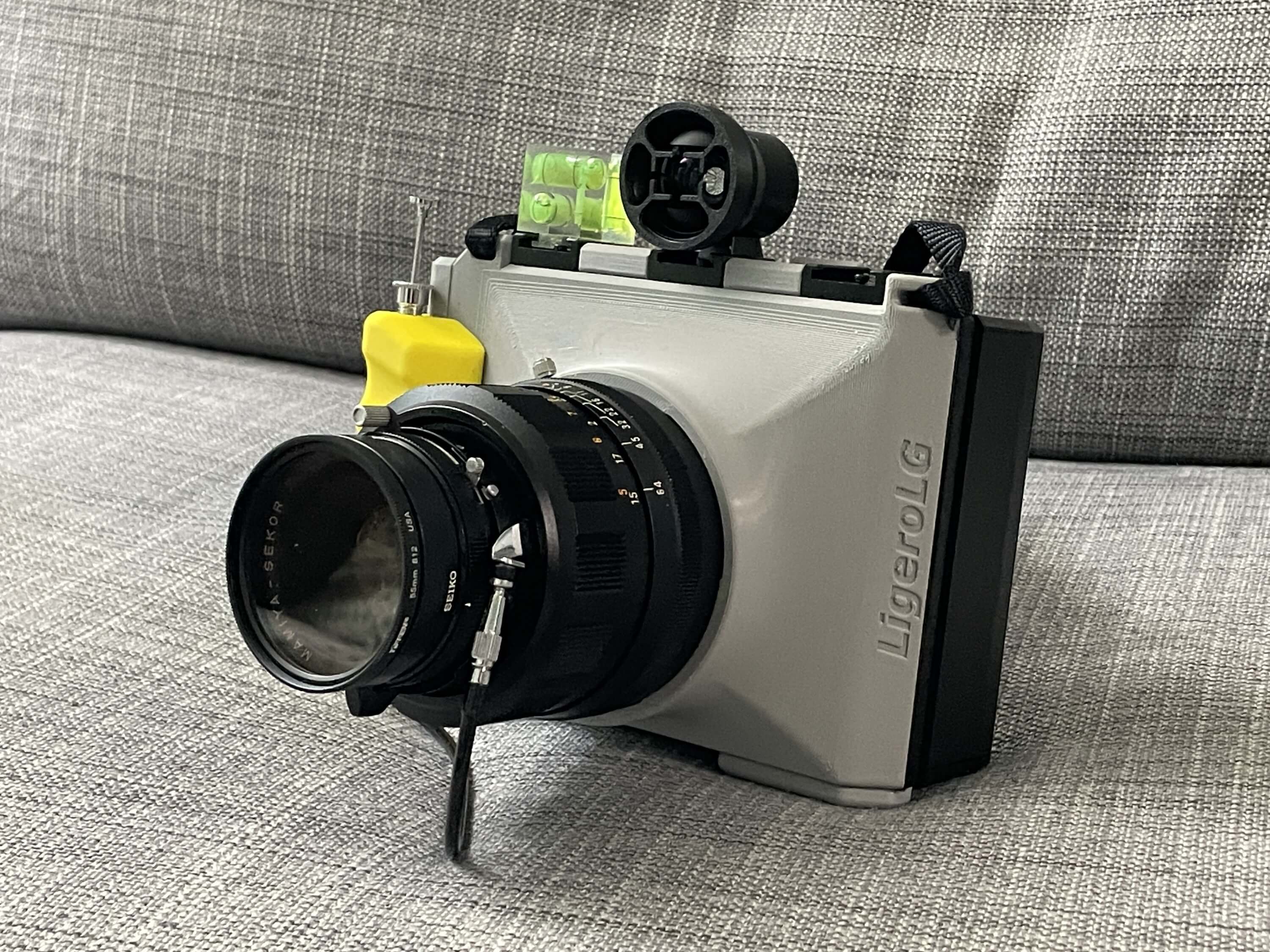 LigeroLG camera, printed in grey and yellow, attached to a Lomograflok back, with a viewfinder and flash attached to the top, sitting on a table