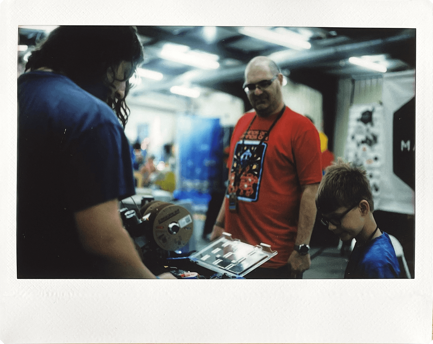 Instax Wide print of two adult men and one young boy looking at a 3D printer at Maker Faire 2024
