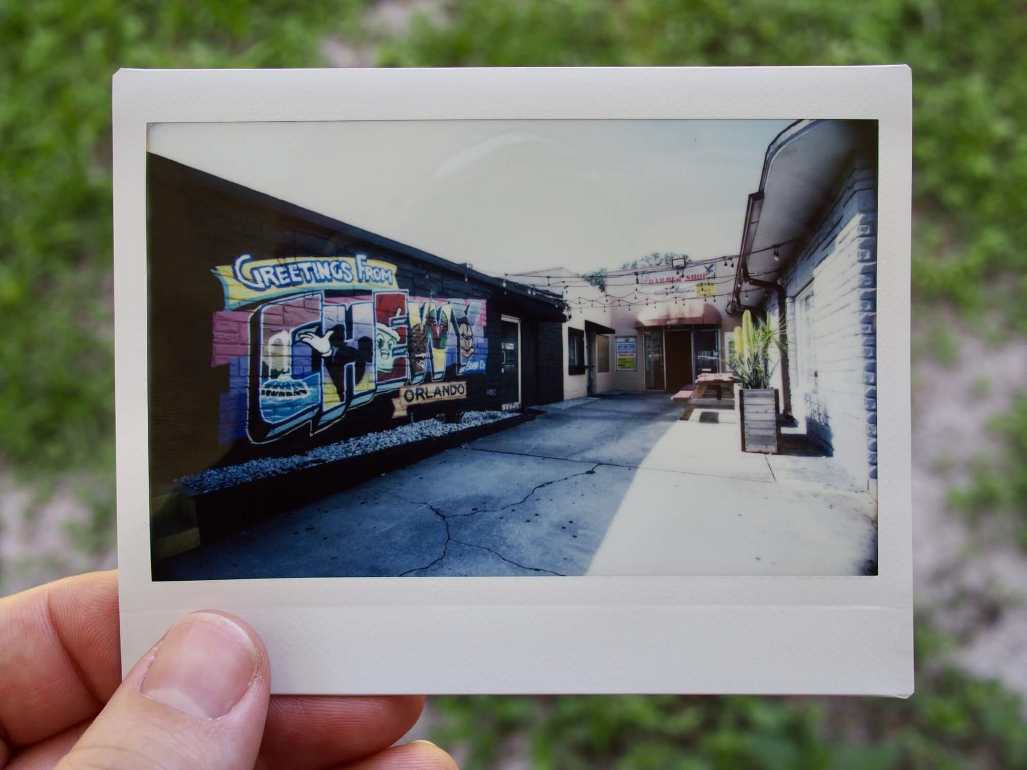 Wide angle Instax Wide print with the Chewy Boba Orlando mural on the left, an alleyway in the middle, and a wall on the right